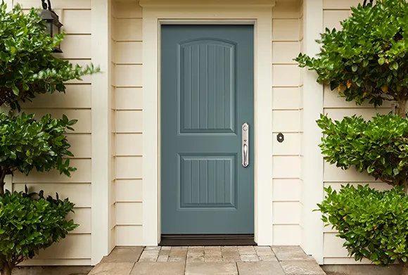 Inviting home entrance with a blue front door, beige exterior walls, and neatly trimmed green plants on either side.