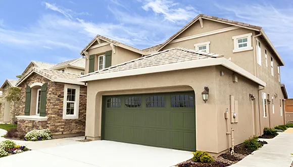 Beige two-story suburban house with a double garage, manicured front yard, and a clean driveway.